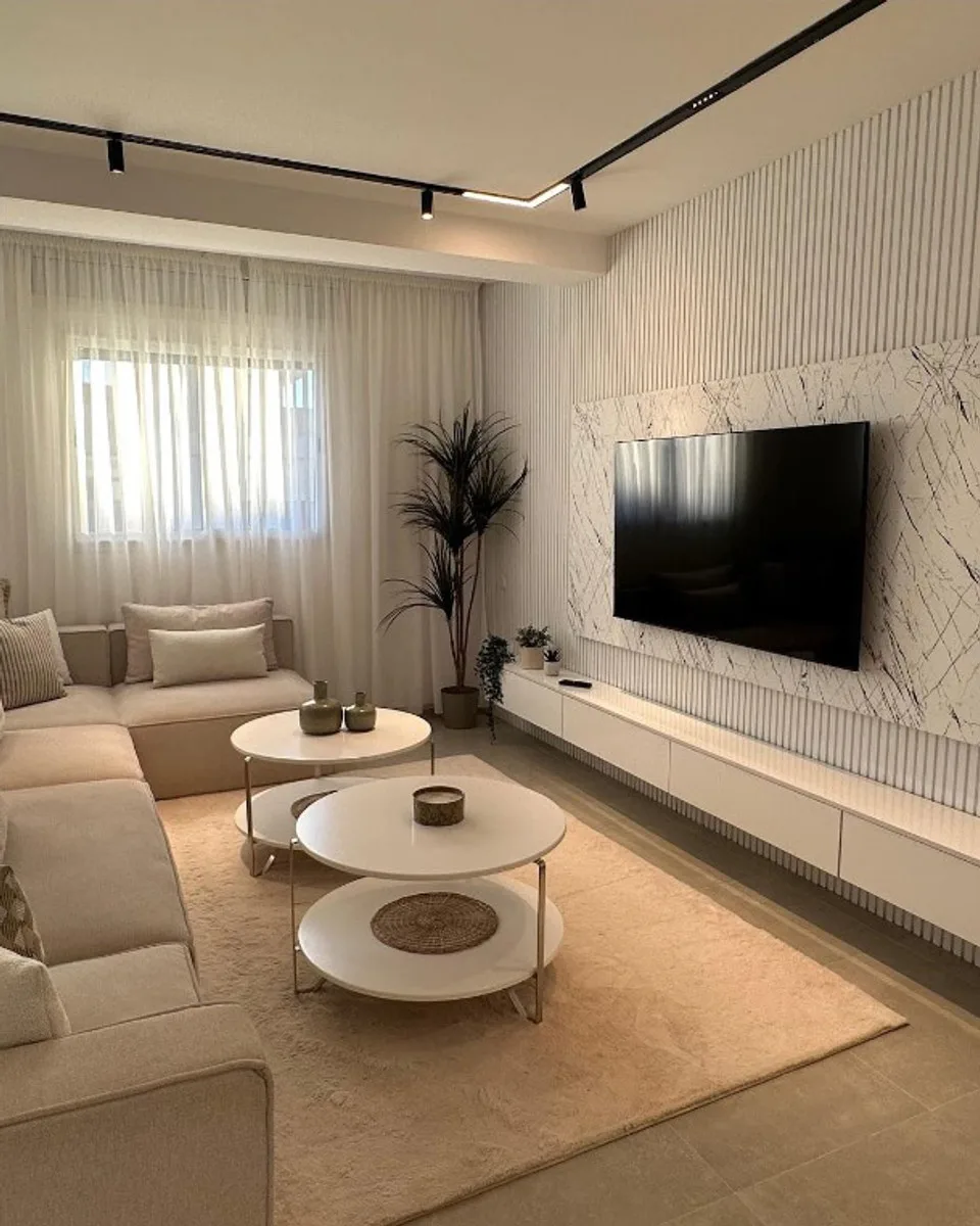 Le salon de l'Appartement Star : canapés clairs, tables basses rondes et mur télévision blanc.