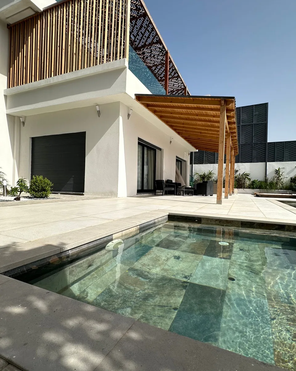 La Villa Élite : façade blanche, pergola en bois et piscine en pierre verte.