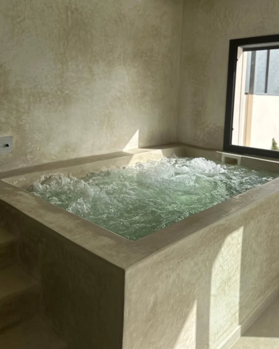 Le spa de la Villa Gris Montaigne : jacuzzi en enduit beige, face à une fenêtre.