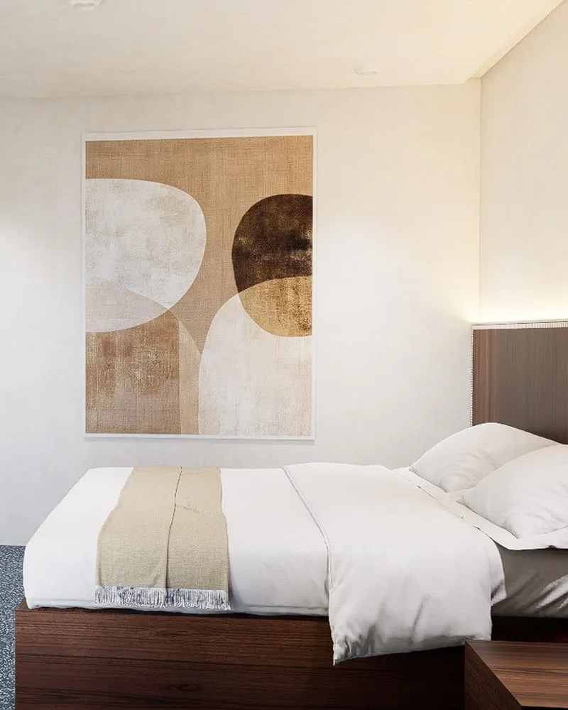 Une chambre de l'hôtel : lit blanc, tête de lit en bois sombre et grand tableau aux tons ocre.